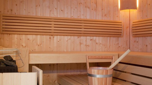 A cozy sauna made of light wood with benches and a bucket for water. Soft lighting creates a relaxing atmosphere. - Appartement Alpin - Sölden