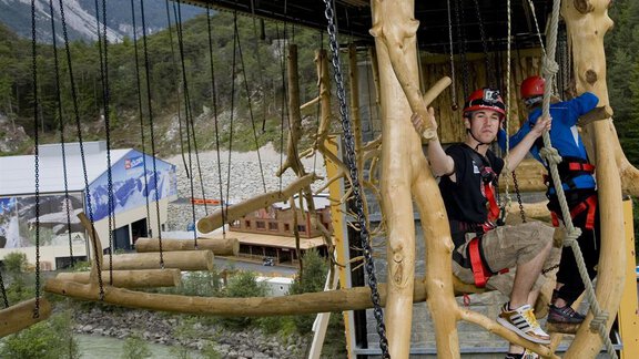 A climbing park in nature with two people swinging in safety gear. Trees and a building can be seen in the background. - Appartement  Fabio - Sölden