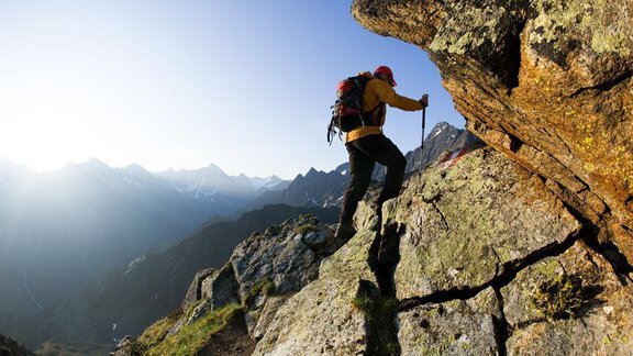 A hiker climbs a rocky slope in the mountains. The surroundings are characterized by majestic peaks and clear skies. - Appartement  Fabio - Sölden