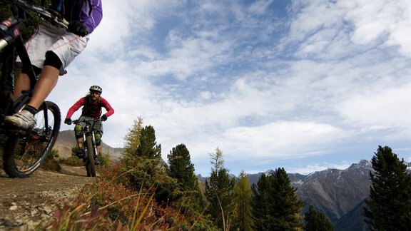 Two mountain bikers ride along a narrow path. In the background, mountains and a blue sky are visible. - Appartement  Fabio - Sölden