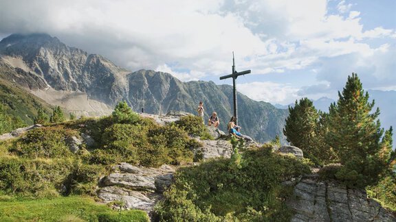 A picturesque mountain landscape with a wooden cross on a summit. In the background, tall mountains and a cloudy sky can be seen. - Appartement  Fabio - Sölden