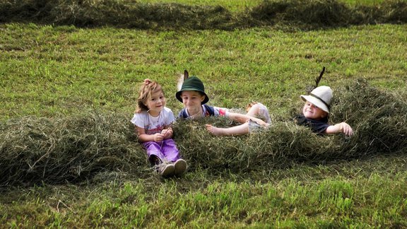 Three children are happily sitting in a freshly mowed field. They are surrounded by hay and are enjoying the day in nature. - Appartement  Fabio - Sölden