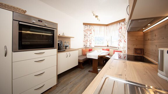A modern kitchen with bright cabinets and wood paneling. The dining area is cozy with a table and a bench. - Appartement Harmonie - Sölden
