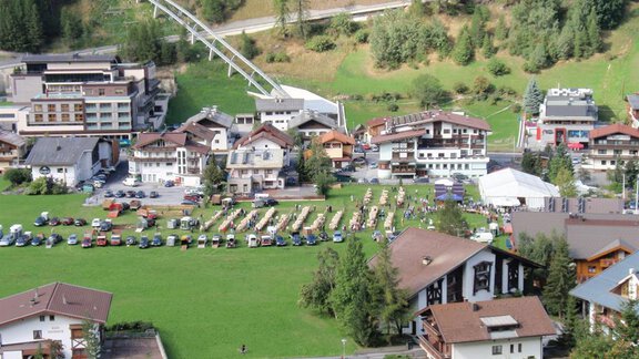 A picturesque town with several buildings and a green field. On the field, there are many cars and loungers. - Appartement Schwalbennest - Sölden