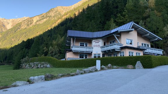 A large, modern building surrounded by mountains and forests. The sky is clear and the surroundings are green and inviting. - Appt. Ideal - Sölden