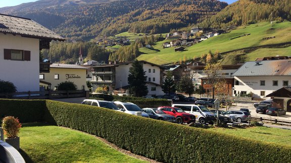 A picturesque landscape with gentle hills and beautiful mountains in the background. In the foreground, there are green lawns and parked cars. - Appt. Ideal - Sölden