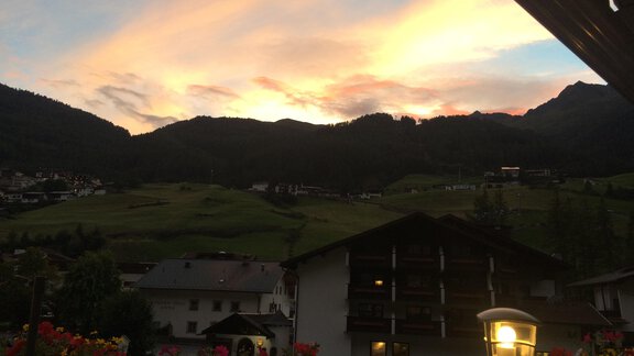 A picturesque sunset over the mountains, with gentle hills and a clear sky. In the foreground, houses and colorful flowers can be seen. - Appt. Ideal - Sölden