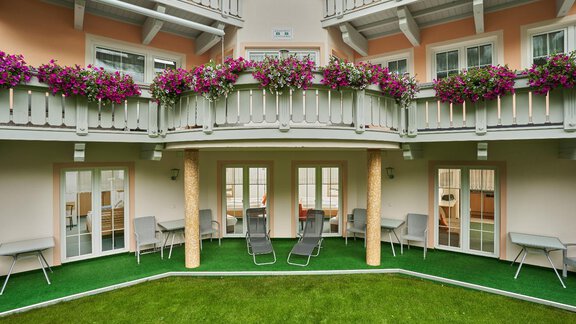 A cozy courtyard with green lawn and modern loungers. Blooming plants adorn the balconies of the building. - Appt. Ideal - Sölden