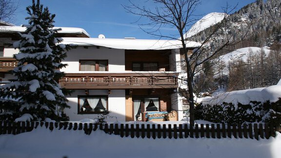A charming house in the snow with a balcony and windows that radiate warmth. Snow-covered mountains are visible in the background. - Appt. Schnöller - Sölden
