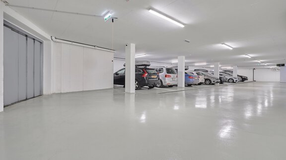 Eine helle Tiefgarage mit mehreren geparkten Autos. Der Boden ist glänzend und die Wände sind weiß. - Bäckelar Wirt - Sölden