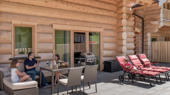 A cozy terrace with a wooden house in the background. A family is sitting together and enjoying the time in the sunshine. - Chalet Resort Sölden - Sölden