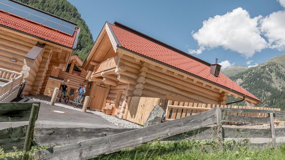 A modern log cabin with red roofs in a mountain landscape. In the foreground, there is a wooden fence and a meadow. - Chalet Resort Sölden - Sölden