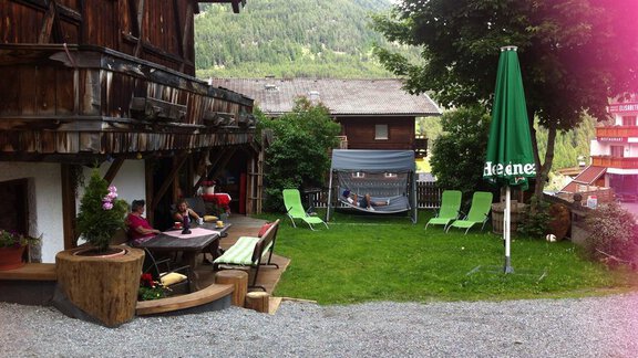 A cozy garden with loungers and a pavilion. In the background, there is a traditional wooden house and green mountains. - Erbhof - Sölden