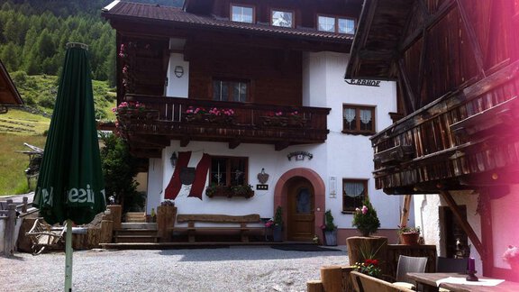 A traditional alpine house with wooden-decorated balconies and colorful flowers. The outdoor area offers seating and a peaceful, rural setting. - Erbhof - Sölden