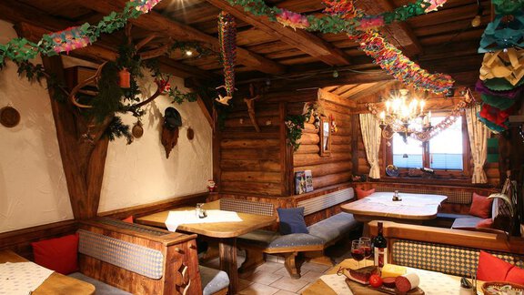 A cozy restaurant with wooden paneling and rustic tables. Colorful decorations and an inviting atmosphere create a pleasant ambiance. - Erbhof - Sölden