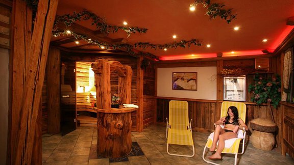 A relaxing wellness area with wooden paneling. A woman is sitting in a lounge chair, enjoying the calm atmosphere. - Erbhof - Sölden