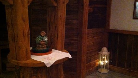 A rustic wooden well stands in a cozy room. Next to the well, there is a figurine statue on a white cloth. - Erbhof - Sölden