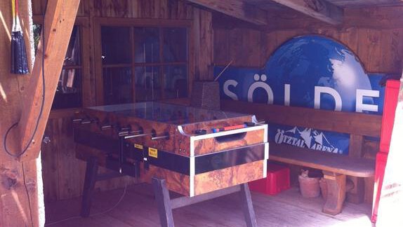 A cozy cabin with a foosball table and wooden paneling. In the background, there is a large sign that says "Sölden." - Erbhof - Sölden