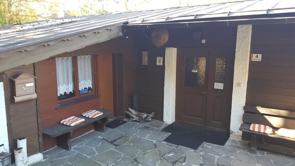 A cozy wooden house with an entrance and a small porch. Benches are outside and the ground is made of stone slabs. - Ferienhaus Anna - Sölden