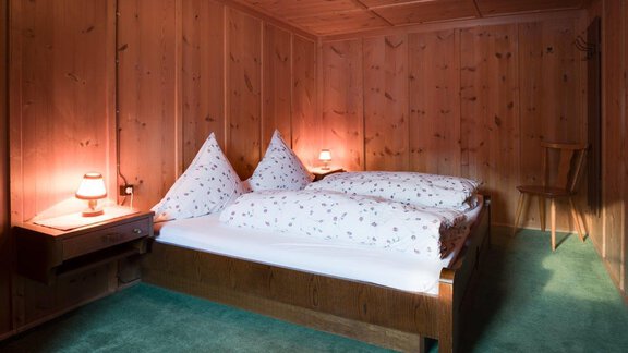 A cozy bedroom with wooden paneling and a double bed. The lighting creates an inviting atmosphere. - Ferienhaus Karlingerhof - Sölden