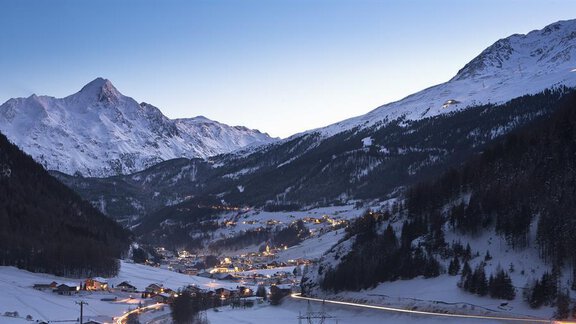 A picturesque mountain village in the snow at dusk. The surrounding mountains are majestic, and warm lights glow from the houses. - Ferienhaus Karlingerhof - Sölden
