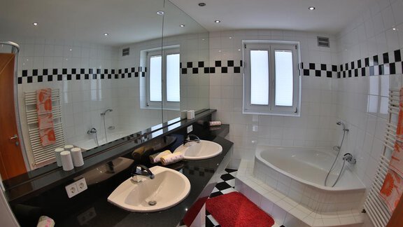 A modern bathroom with two sinks, a bathtub, and an elegant design in black and white. The walls are tiled, and the light is bright and inviting. - Ferienhaus Moidl - Sölden