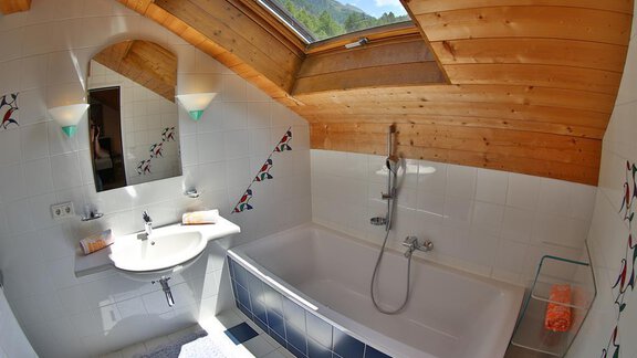 A bright bathroom with a bathtub and a sink. The wooden beam ceiling and the window create a cozy atmosphere. - Ferienhaus Moidl - Sölden