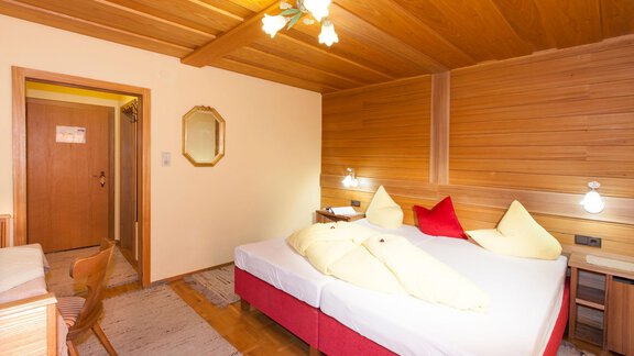 A cozy bedroom with wooden paneling and two beds. The decor is simple and inviting, with a small table and chair. - Gästehaus Kneisl - Sölden