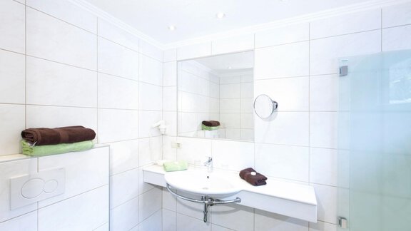 A modern bathroom with a large mirror and an elegant sink setup. Clean tiles and neatly folded towels create an inviting atmosphere. - Gästehaus Kneisl - Sölden