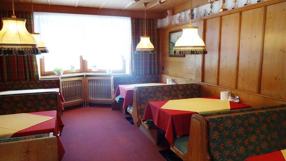 A cozy restaurant with wooden walls and colorful tablecloths. There are comfortable seating areas and a bright window front. - Gästehaus Marco - Sölden