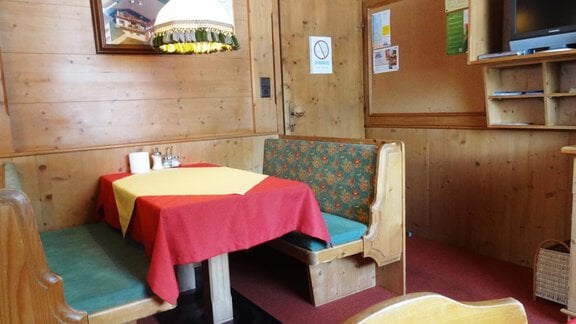 A cozy corner bench in a rustic room with wood paneling. The table is set with a yellow and red tablecloth. - Gästehaus Marco - Sölden