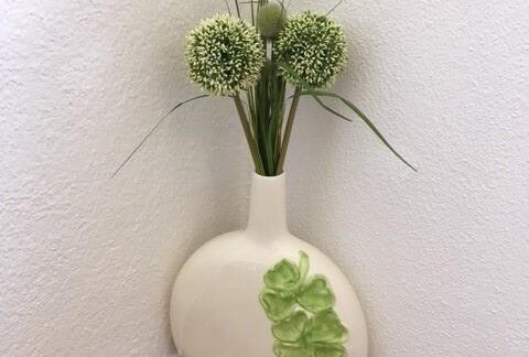 An elegant vase shaped like a pear with a green decoration. Inside are artificial flowers and grass arrangements in fresh shades of green. - Gästehaus Marco - Sölden