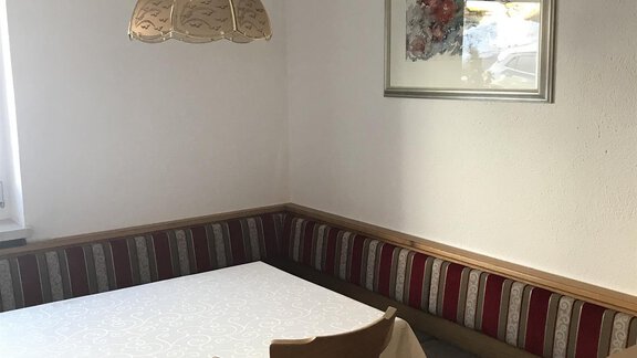A cozy dining area with a table and a bench. A ceiling light and an artistic picture on the wall give the room an inviting atmosphere. - Gästehaus Martin - Sölden