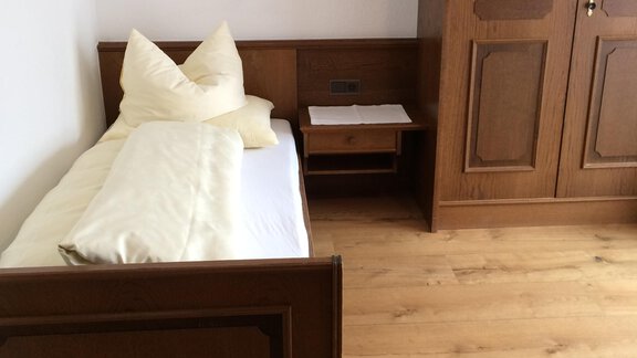 A simple bedroom with a wooden bed and a dresser. The floor is made of wood and the walls are white. - Gästehaus Martin - Sölden