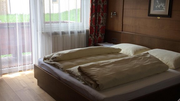 A cozy bedroom with a large bed and wooden floor. Large windows let in plenty of natural light. - Gästehaus Martin - Sölden