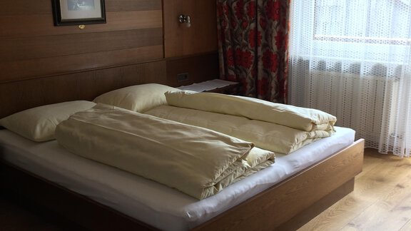 A cozy bedroom with a double bed and wooden paneling. The windows let in plenty of daylight, and the room feels inviting and warm. - Gästehaus Martin - Sölden