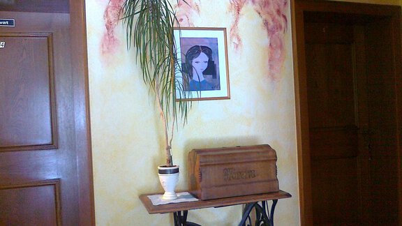 A cozy hallway with two doors and a decorative table. On the table, there is a potted plant and an artistic wooden box, while the wall is designed in warm colors. - Gästehaus Martin - Sölden