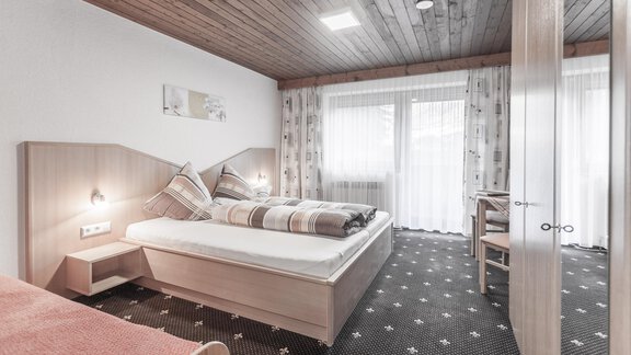 A cozy bedroom with two beds and a wooden ceiling. The room has large windows and a pleasant atmosphere. - Gästeheim Schmiedhof - Sölden