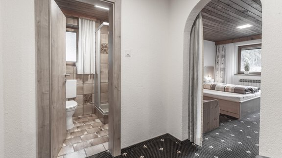 A cozy hallway with a bathroom to the left and a bedroom to the right. The walls are light and the floor has an interesting pattern. - Gästeheim Schmiedhof - Sölden