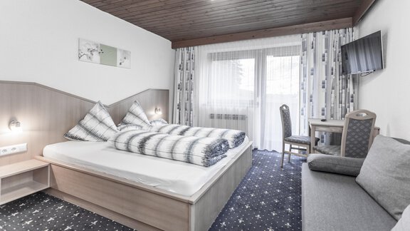 A cozy bedroom with a double bed and a comfortable sitting area. Large windows let in plenty of daylight and offer a view outside. - Gästeheim Schmiedhof - Sölden