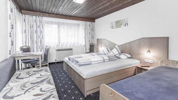 A simple hotel room with two beds and a desk. The walls are light, and there are large windows that let in a lot of light. - Gästeheim Schmiedhof - Sölden