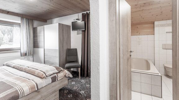 A cozy room with a double bed and a television. In the background, there is a modern bathroom with a bathtub. - Gästeheim Schmiedhof - Sölden
