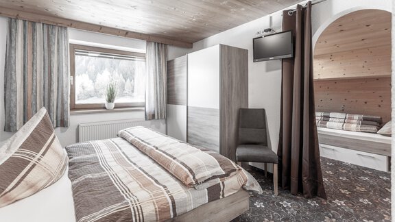 A modern bedroom with a double bed and a cozy seating area. Large windows provide plenty of natural light and a pleasant atmosphere. - Gästeheim Schmiedhof - Sölden
