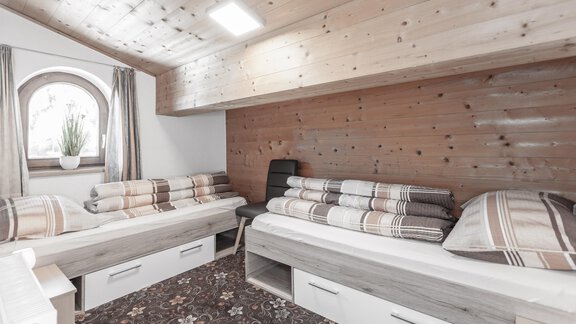 A cozy bedroom with wooden paneling and two single beds. The room has a large window that lets in natural light. - Gästeheim Schmiedhof - Sölden