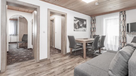 A modern living room with a cozy sofa and a dining table. The rooms are bright and inviting, with wooden floors and windows that let in daylight. - Gästeheim Schmiedhof - Sölden