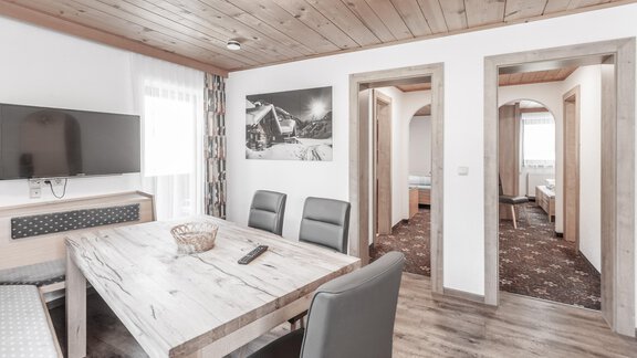 A modern and inviting living room with a large table and stylish chairs. In the background, two doors to other rooms are visible. - Gästeheim Schmiedhof - Sölden