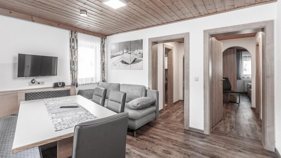 A modern living room with a gray couch and a dining table. The walls are light and the wooden floor provides a cozy atmosphere. - Gästeheim Schmiedhof - Sölden