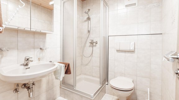 A modern bathroom with a shower, a sink, and a toilet. The walls are light tiled, and the room feels clean and inviting. - Gästeheim Schmiedhof - Sölden