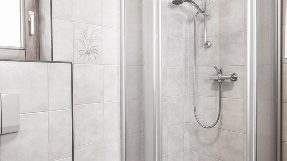 A modern shower in a bright bathroom. The walls are lined with white tiles and there is a window that lets in light. - Gästeheim Schmiedhof - Sölden