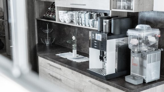 A modern kitchen with a coffee machine and a water station on the countertop. In the background, plates and cups are visible in a shelf. - Gästeheim Schmiedhof - Sölden